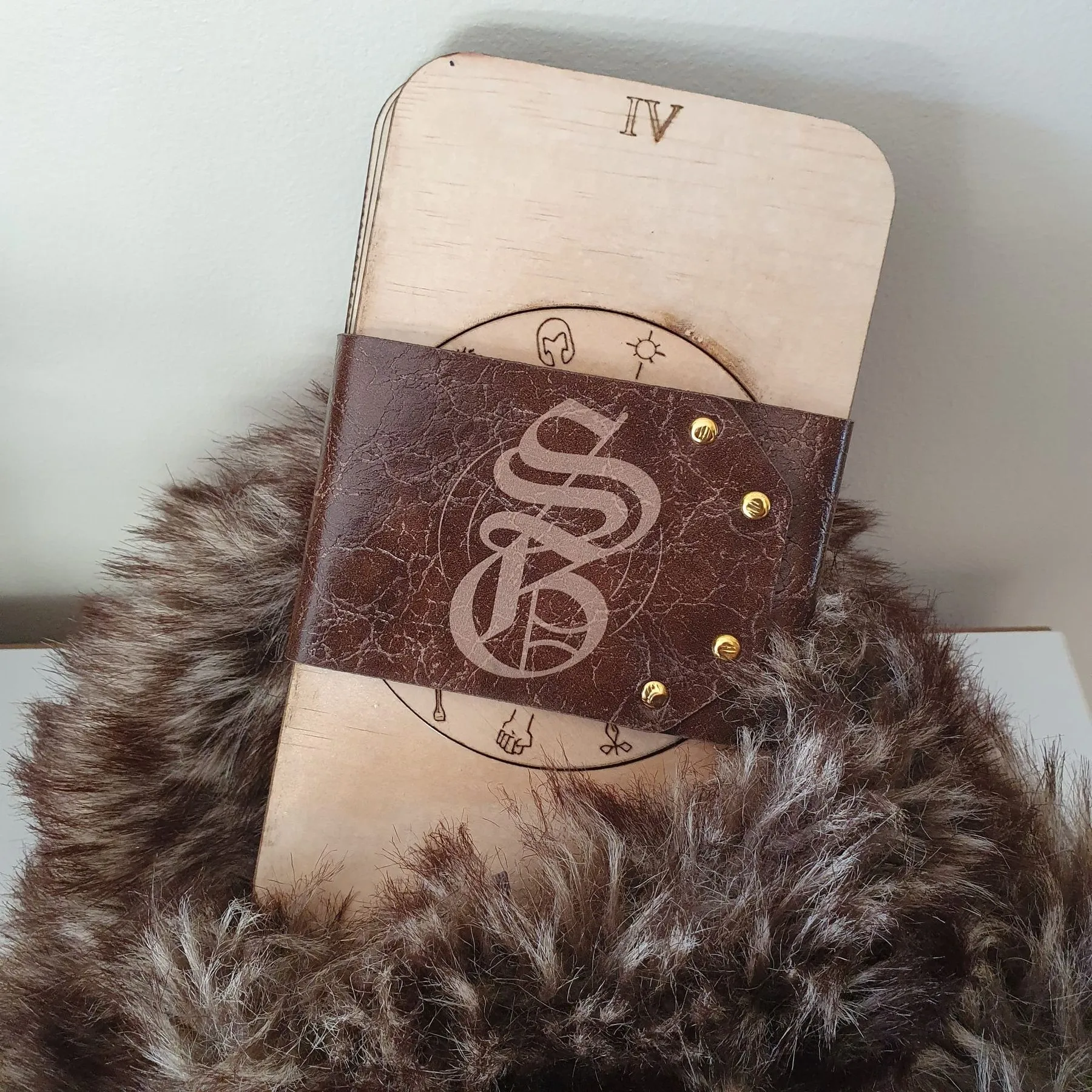 The Summoner's Grimoire closed, a wooden case bound with a studded faux-leather strap, resting on fur